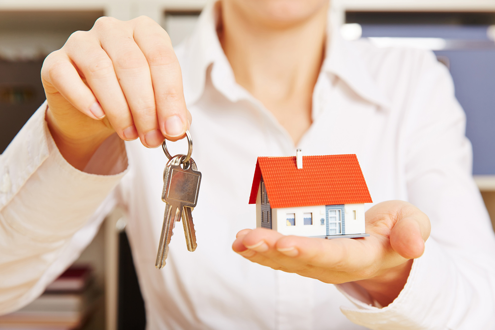 A woman holding a key and a house miniature